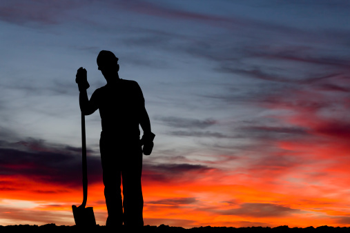 A royalty free image from the construction industry of a construction worker at a construction site holding onto his shovel.