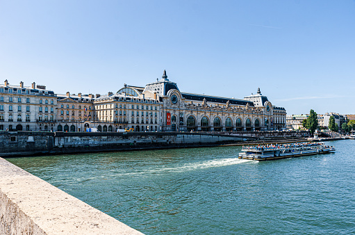 Paris, France - Aug 22, 2019.
Photographed from Pont Royal.  Boats carrying tourists can be seen on the Seine River.

The museum holds mainly French art dating from 1848 to 1914, including paintings, sculptures, furniture, and photography.