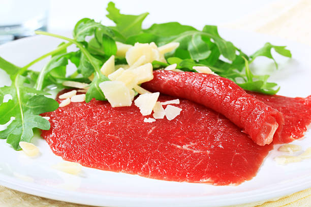 fette di carpaccio guarnito con parmezan e rucola - beef carpaccio foto e immagini stock