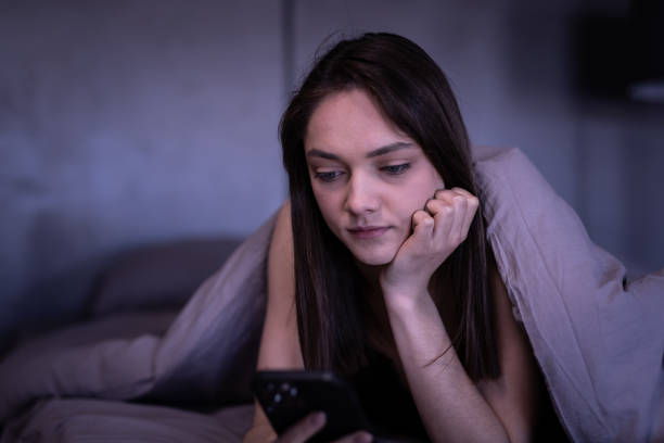 istock Sleepy woman lying in bed under the blanket using phone at night 1700050578