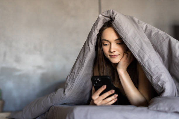 istock Sleepy woman lying in bed under the blanket using phone at night 1700053368