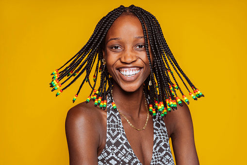 Portrait of a beautiful young happy smiling african american woman with dread hair isolated over yellow background at studio.