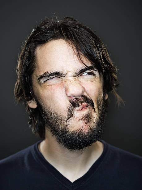 Young man grimacing Portrait of a young man with a beard winking and making a face. ugly face stock pictures, royalty-free photos & images
