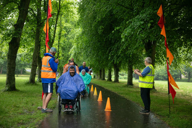 A shot of a group of run participants taking part in a fun run in Leazes Park in Newcastle upon Tyne, North East England. An adult male in a wheelchair is crossing the finish line with the help of a friend as two volunteers cheer them on and record finishing times. The race is open to people of all ages and abilities and is also dog friendly.\n\nThese files have similar videos/images available.