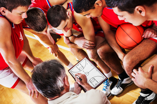 Basketball players looking at the coach drawing a strategy.   