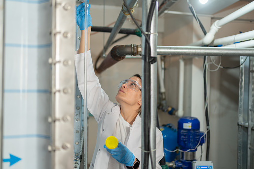 Female Quality Control Specialist Sampling Water From The Water Storage Tank In A Basement