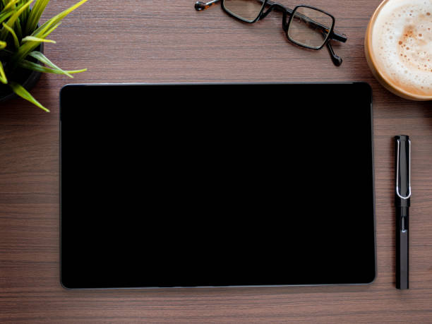 istock Template, mock-up digital tablet pc computer with blank black screen and pen, coffee cup, glasses, little tree on brown workplace. Top view, flat lay. 1700076293