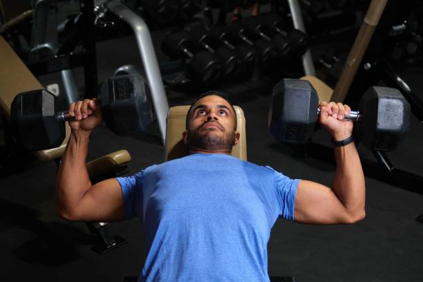 Strong Latin man doing dumbbell chest press at a gym. stock photo