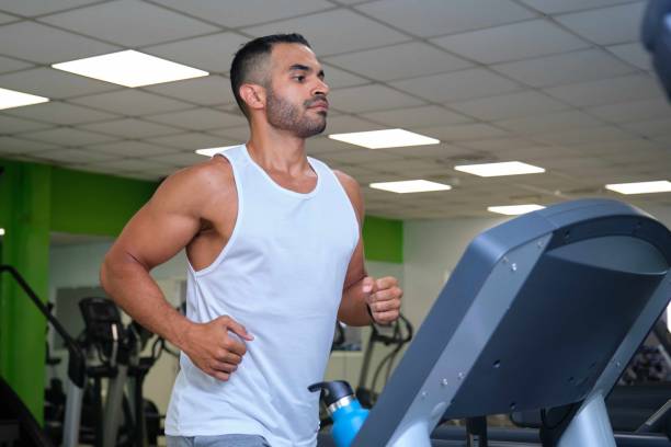 Strong Latin man running on treadmill at a gym. stock photo