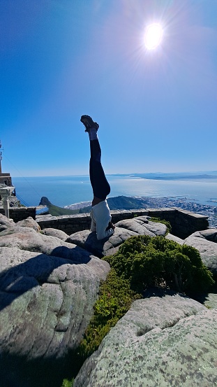 A young woman doing a headstand on the table mountain in South Africa