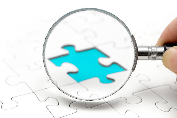 Searching the Missing Piece Human hand holding a magnifying glass and searching for a missing puzzle piece. Selective focus. spy games stock pictures, royalty-free photos & images