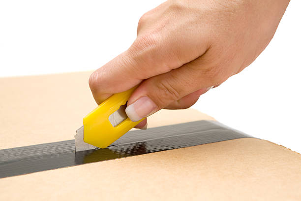 Woman opening a box with a yellow cutter in her hand. Isolated on a white background.