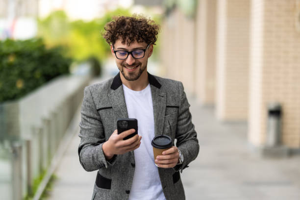 istock Bearded businessman in formal suit on break using mobile phone use smartphone with coffee cup in downtown outdoors. 1700114459