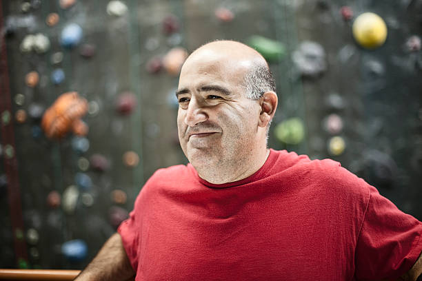 Mature Adult Male Taking a Break at the Gym Mature adult male relaxing at the gym. Rock climbing wall in the background.  60 69 years stock pictures, royalty-free photos & images