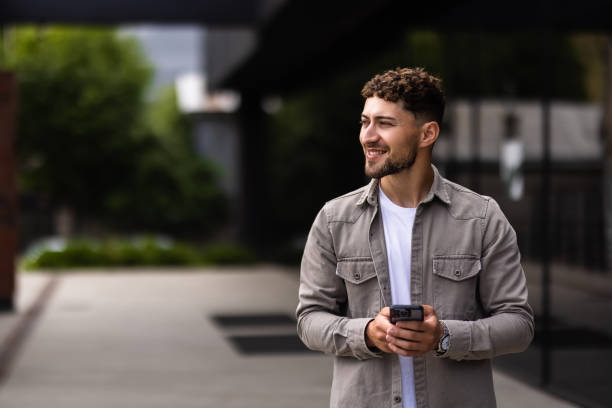 istock Confident young man using cell phone and drinking coffee in the city 1700121071