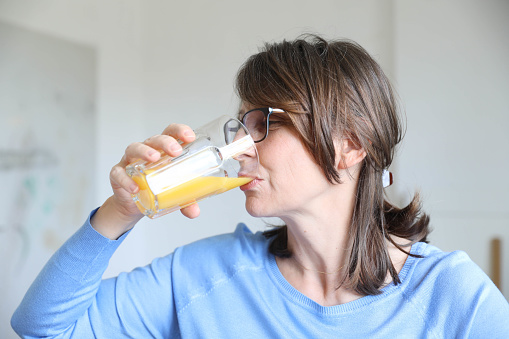 Elderly woman drinking fresh juice in the kitchen