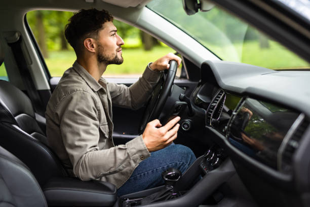 istock A young man driving his own car uses a smartphone or phone. Multitasking concept 1700136682