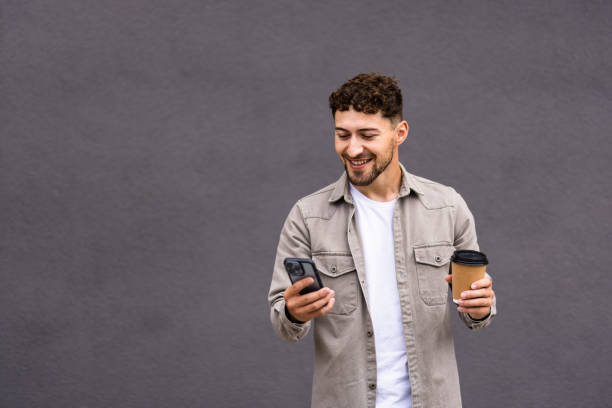 istock Young man using smartphone drinking coffee at street 1700140496