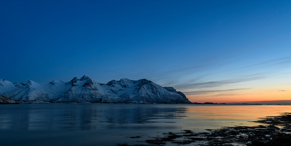 Snowy winter landscape during sunset at the shore of the Austvågøy island of the Lofoten archipel in Northern Norway The mountains are covered in snow. Long exposure image.