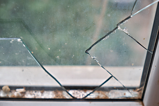 Broken glass in a plastic window in a house, on a green background. Broken glass, cracks in the glass.