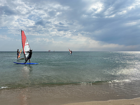 Gokceada, Canakkale Turkey September 9, 2023; Wind surfers enjoying the Aegean sea and the wind  in Gokceada Kefalos bay against the clear sky. Imbros Island.