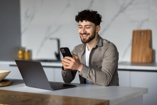 istock Handsome man using mobile phone while sitting with laptop at the table at home 1700182354