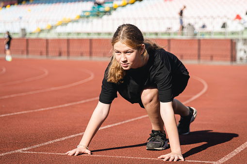 Athlete teenager preparing before jogging running, stretching legs before workout training outdoors on stadium in the morning.