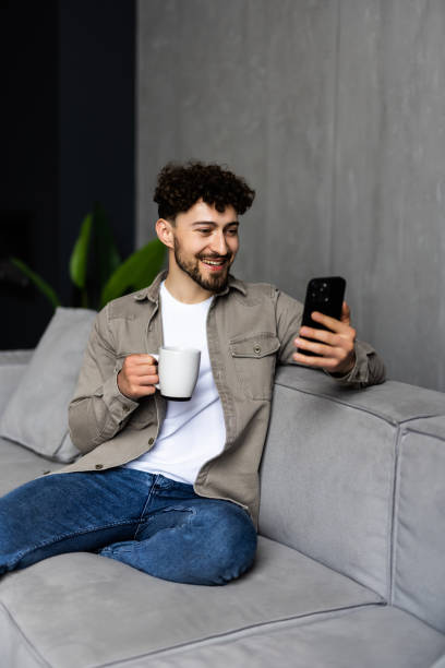 istock Happy man sitting in living room on couch at home chatting typing email message using cellular. 1700192164