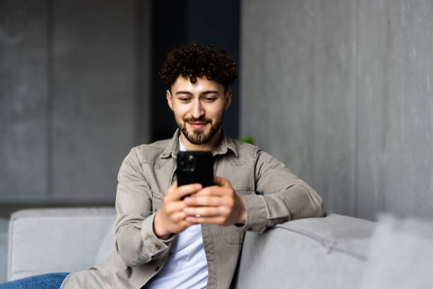 istock Content young man relax on sofa use smartphone spend free time online in social network chat at web app play easy game online. 1700192765