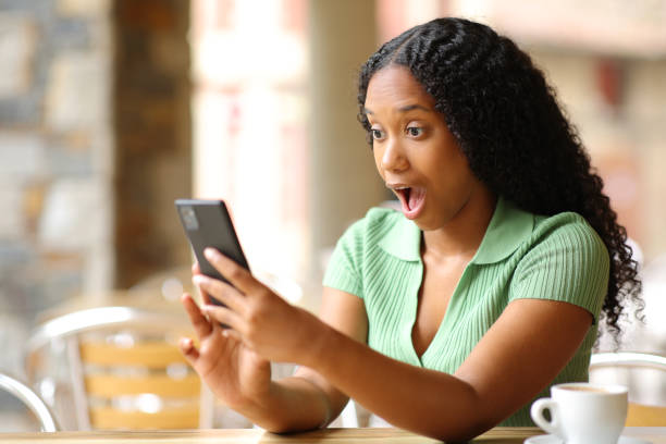 istock Amazed black woman checking smart phone in a bar 1700197234