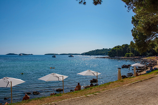 Rovinj, Croatia - July 8th 2023. White beach umbrellas on the coast at Cuvi Beach just south of Rovinj old town in Istria, Croatia