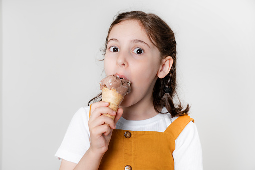 Caucasian litlle Girl in white T-shirt Holding Donut with pink glaze on white background. The girl smiles and looks at the camera