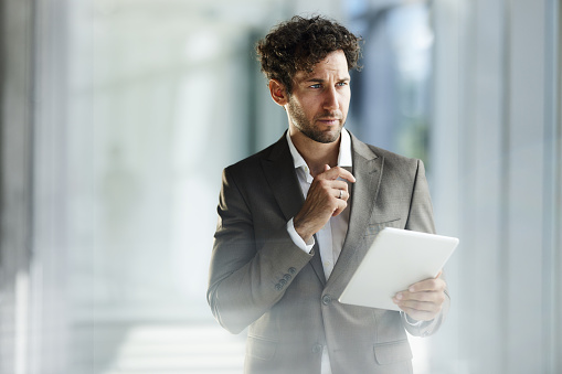 Young businessman brainstorming while working on digital tablet in a hallway of an office building. Copy space.