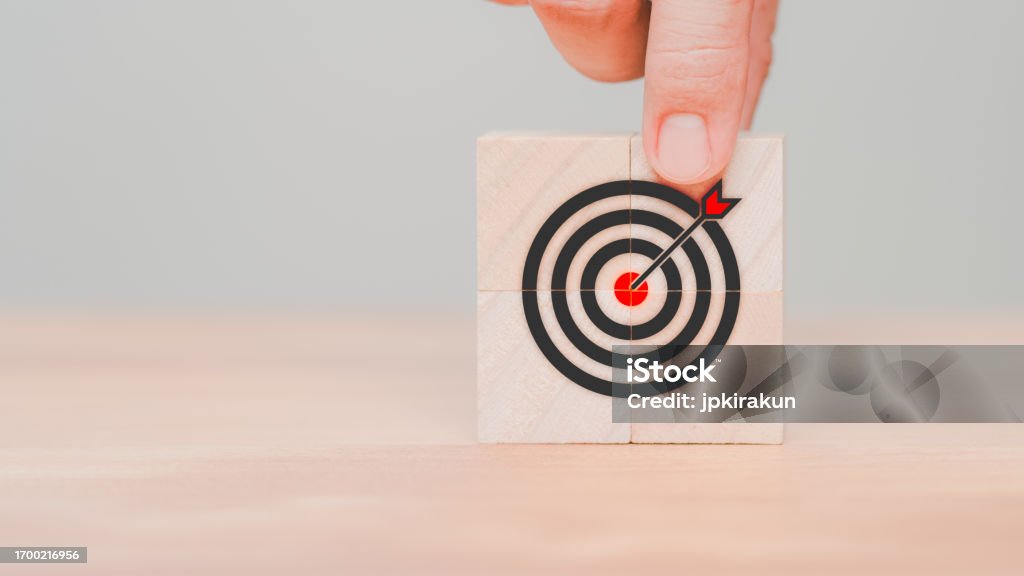 Hand put a goal icon on wooden cube block on wood table. Business concept of growth and goals in next year, targets, objectives, business success, planning, achievement, KPI and OKR. Achievement Stock Photo