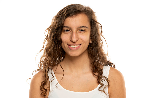 Portrait of a young smiling woman without makeup and long wavy hair on a white studio background