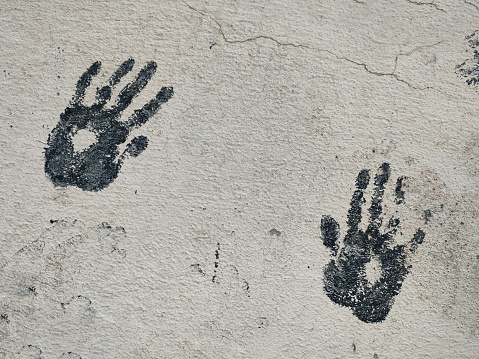Pair of black prints of children's palms diagonal arrangement on gray concrete wall, copy space, close-up