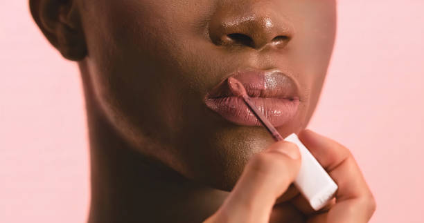 Visagiste applying lip gloss while doing makeup on black transgender model stock photo