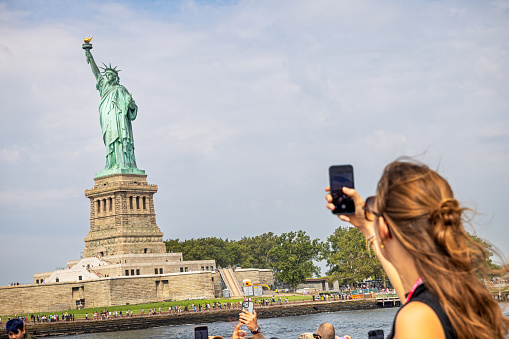 Statue of Liberty, Manhattan, New York, USA - August 12th 2023:  People taking photographs of the Statue of Liberty with their mobile phones