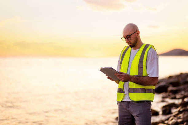 istock Inspection environmentalist. Volunteer man wearing vest and glasses using tablet for analyzing water. Copy space. Concept of air and ocean pollution 1700242553