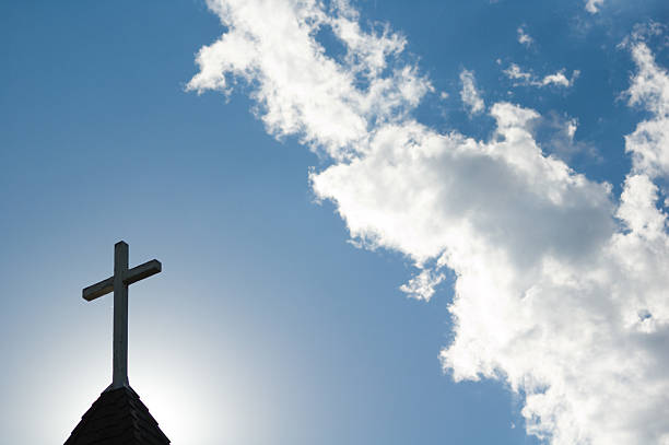 Sunlit Cross and Steeple An old church steeple backlit by a low setting sun. evangelic stock pictures, royalty-free photos & images