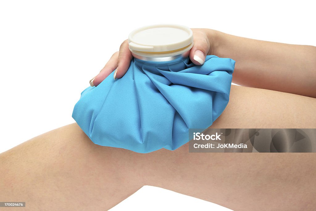 Ice Pack on Knee Joint Woman icing her injured knee with a blue ice pack. Isolated on a white background. Ice Pack Stock Photo
