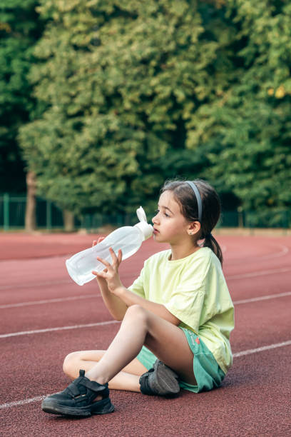 istock Thirsty little girl drinks water while sitting on the stadium. 1700247553