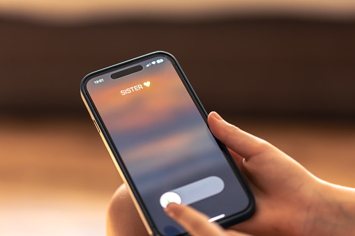 Close up of child hands holding phone with sister incoming call on display on a blurred background.