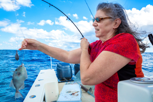 Older woman catching a fish on a boat in the ocean.  rr