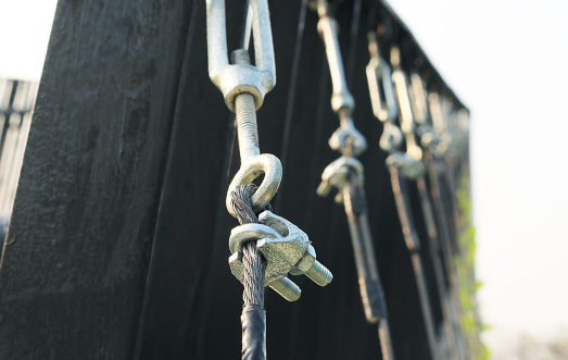 Closeup wire rope socket with anchor pendant installed on steel fence railing.