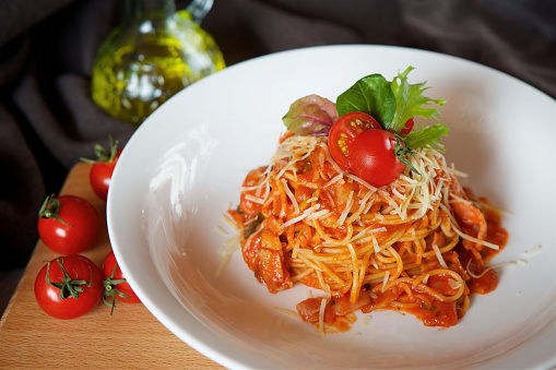 Pasta with red sauce, tomatoes and basil. Served on a white plate with herbs.