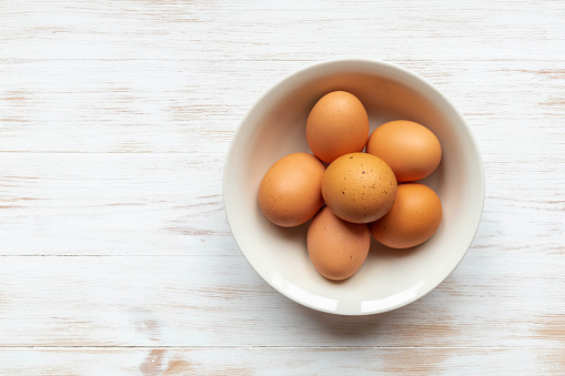 Plate with brown chicken eggs on wooden table. Brown eggs in bowl on wood background. Free-range organic eggs in bowl. Natural healthy food concept. Top view, flat lay, copy space.
