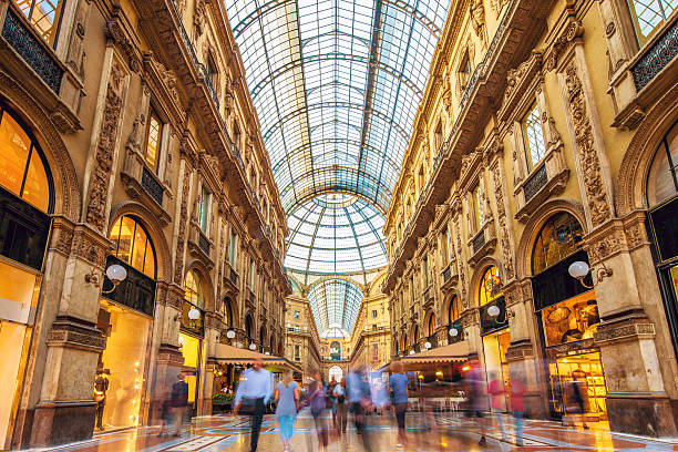 Galleria Vittorio Emanuele II in Milan, Italy Shot of the famous Galleria Vittorio Emanuele II in Milano, Italy, the famous luxury shopping mall, showing the spectacular view of an almost golden gate to luxury. Long exposure with motion blurred people walking along the shops and restaurants. Milan, Lombardy, Italy milan stock pictures, royalty-free photos & images
