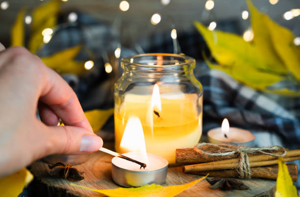 istock A woman's hand lights a candle with a match. Warm autumnal composition. Selective focus. 1700276717