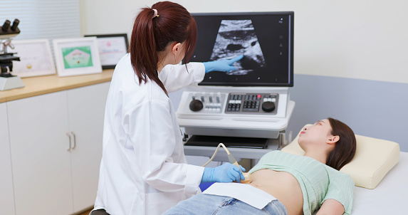 asian doctor using ultrasound scanner performing examination of  belly for her patient - feminine health medical concept